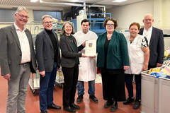 Gruppenfoto von der Bescheidübergabe vor der Faltmaschine