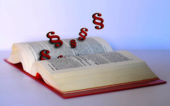 Aus einem aufgeschlagenen Gesetzbuch fliegen rote Paragraphenzeichen.